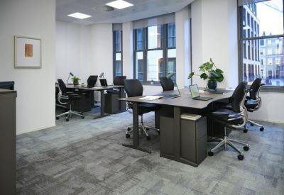 Sunlit office suite with several modern desks, ergonomic chairs, and large windows.