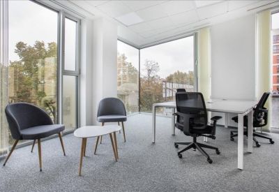 Open-plan workspace with a small lounge area and desks near a glass corner wall.