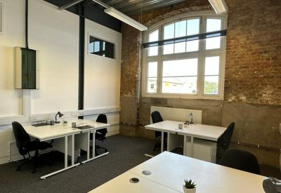 Private office suite with white desks and a large arched window against a brick wall.