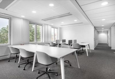Spacious communal coworking area with multiple white desks and large windows.