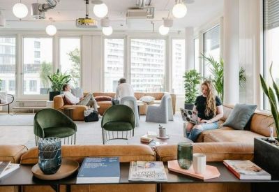 Bright communal lounge with leather sofas, green velvet chairs, and large windows.