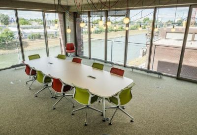 Light-filled meeting room with a large table, vibrant green and red chairs, and views of the canal.