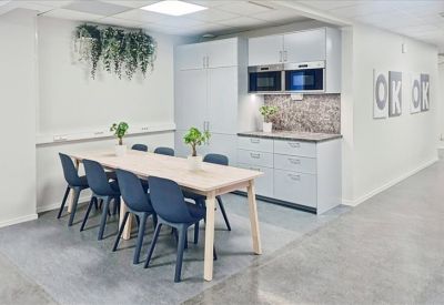 Modern communal kitchen and dining area with light wood table and blue chairs.
