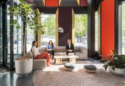 Stylish lobby lounge with grey sofas, large indoor trees, and bright red accent walls.
