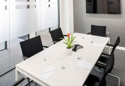 Minimalist meeting room with a white table, black chairs, and a potted plant.