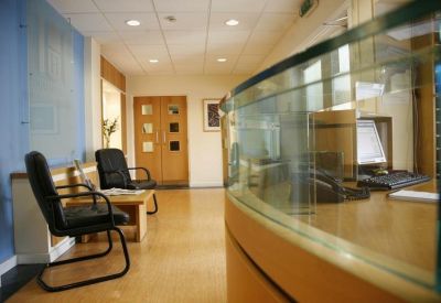 Bright reception area with a curved wooden front desk and black guest chairs.