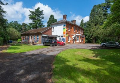 Wide view of the brick building exterior and driveway surrounded by mature trees.