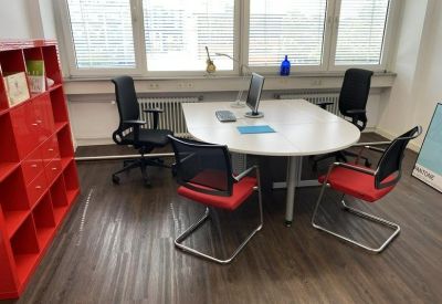 Small meeting room with a round white table, red accent chairs, and a bold red storage shelf.