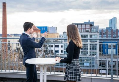 Man and woman conversing on an outdoor rooftop terrace with views of the city skyline.