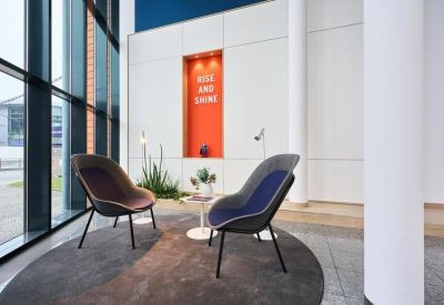 Modern breakout lounge featuring stylish armchairs, a colorful feature wall, and tall windows.