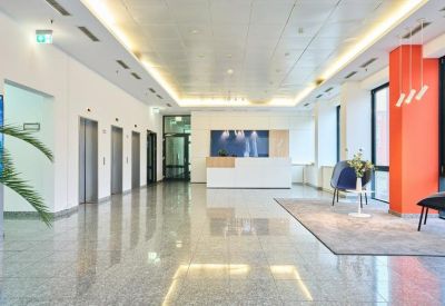 Bright reception area with polished floors, marble-look front desk, and a bold orange feature pillar.