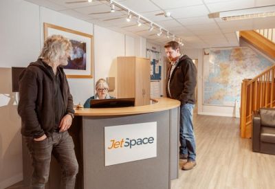 Branded reception area with a curved desk, wooden stairs, and people interacting.