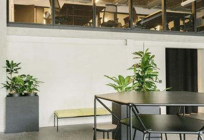 Open-plan office area with black high-top tables and stools beneath a glass-walled mezzanine.