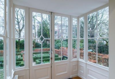 Sunlit communal lounge area with large floor-to-ceiling windows overlooking a manicured garden.