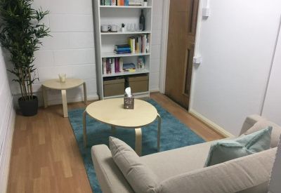 Cozy meeting room with a plush sofa, teal rug, and a tall potted plant.