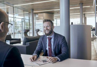 Two men talking in a bright, modern lounge area with floor-to-ceiling windows.
