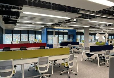 Bright open-plan office with white desks, ergonomic chairs, and colourful privacy screens.