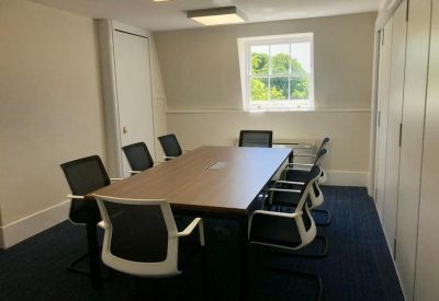Modern meeting room with a wooden table, black-and-white chairs, and views of greenery.