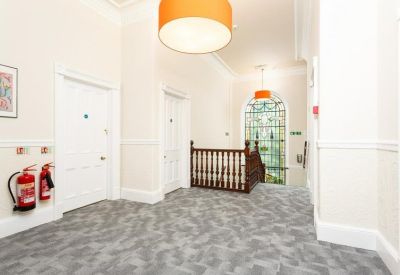 Bright upper hallway with a wooden banister, grey carpet, and orange pendant lighting.