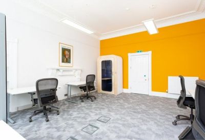 Modern office room with a bright orange feature wall, two desks, and a private phone booth.