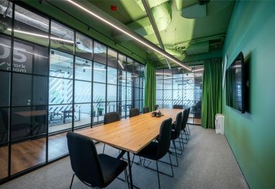 A long wooden boardroom table in a vibrant green room with glass partitions and linear lighting.