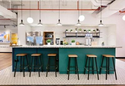 Modern office kitchen and bar area with a teal counter and industrial stools.