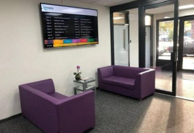 Reception waiting area with two purple sofas and a wall-mounted digital display.