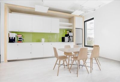 Bright communal kitchen and dining area with a green backsplash and wooden-style chairs.