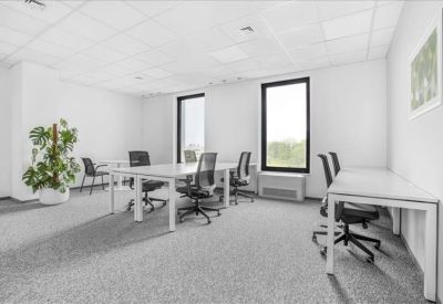 Spacious open-plan office with white desks, ergonomic chairs, and a large potted plant.