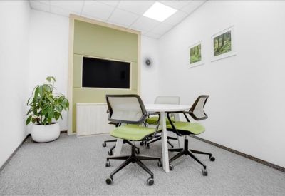 Small meeting room with a round table, green chairs, and a wall-mounted screen.