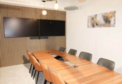 Professional meeting room with a large wooden table and dual wall-mounted screens.