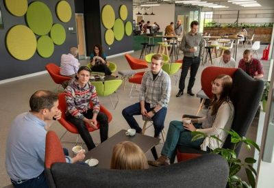 Vibrant communal lounge with green wall circles and people socializing on red and green chairs.