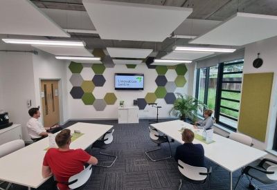 Meeting room with hexagonal wall panels and four people seated around white tables.
