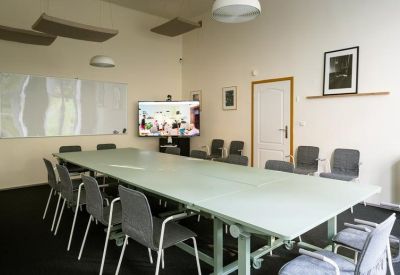 Large conference room with a long table, grey chairs, and a wall-mounted display screen.
