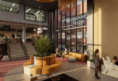 Sunlit lobby lounge featuring a central planter, orange modular sofas, and a reception desk.