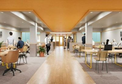 Bright communal coworking space with long wooden tables and warm yellow ceiling accents.