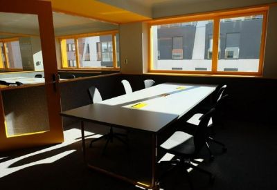 Sunlit meeting room featuring a white table and large yellow-framed windows.