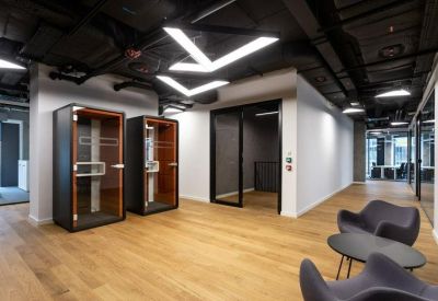 Bright lobby area with wood flooring, grey lounge chairs, and private acoustic phone booths.