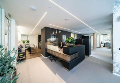 Modern reception area with a dark desk, integrated lighting, and indoor plants.