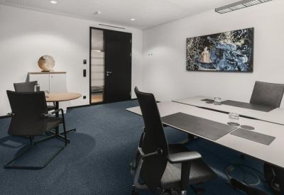 Private office suite featuring a large desk, black ergonomic chairs, and navy blue carpet.