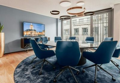 Modern meeting room with blue velvet chairs, a round table, and a large wall-mounted screen.