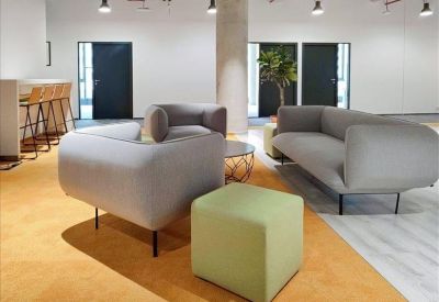 Sunlit communal lounge with grey sofas and a bright yellow carpet.