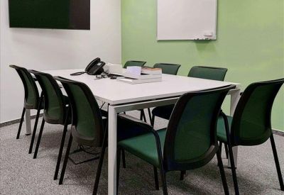 Modern meeting room with a white table, green chairs, and a green accent wall.