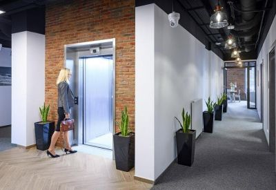 Bright hallway with an elevator, brick accents, and potted plants leading to a workspace.