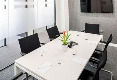 Modern meeting room featuring a white table, black chairs, and a wall-mounted screen.