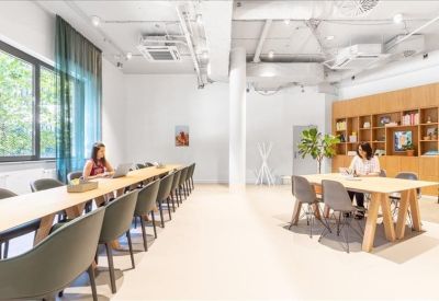 Bright coworking space featuring a long wooden desk with green chairs and floor-to-ceiling windows.