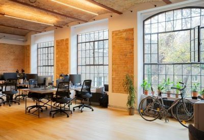 Industrial style open-plan office with brick walls, large windows, and a bicycle.