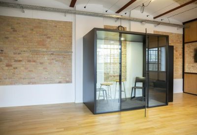 Glass-walled private meeting pod set within an industrial office space.