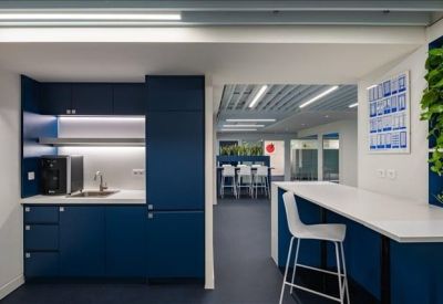 Sleek office kitchenette with navy blue cabinetry, white countertops, and a breakfast bar with high stools.