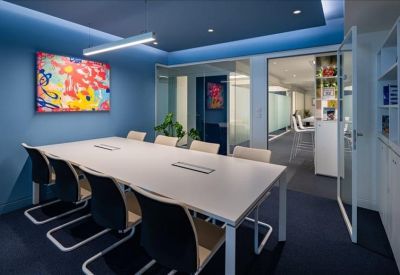 Modern meeting room with a large white table, blue accent walls, and vibrant abstract artwork.